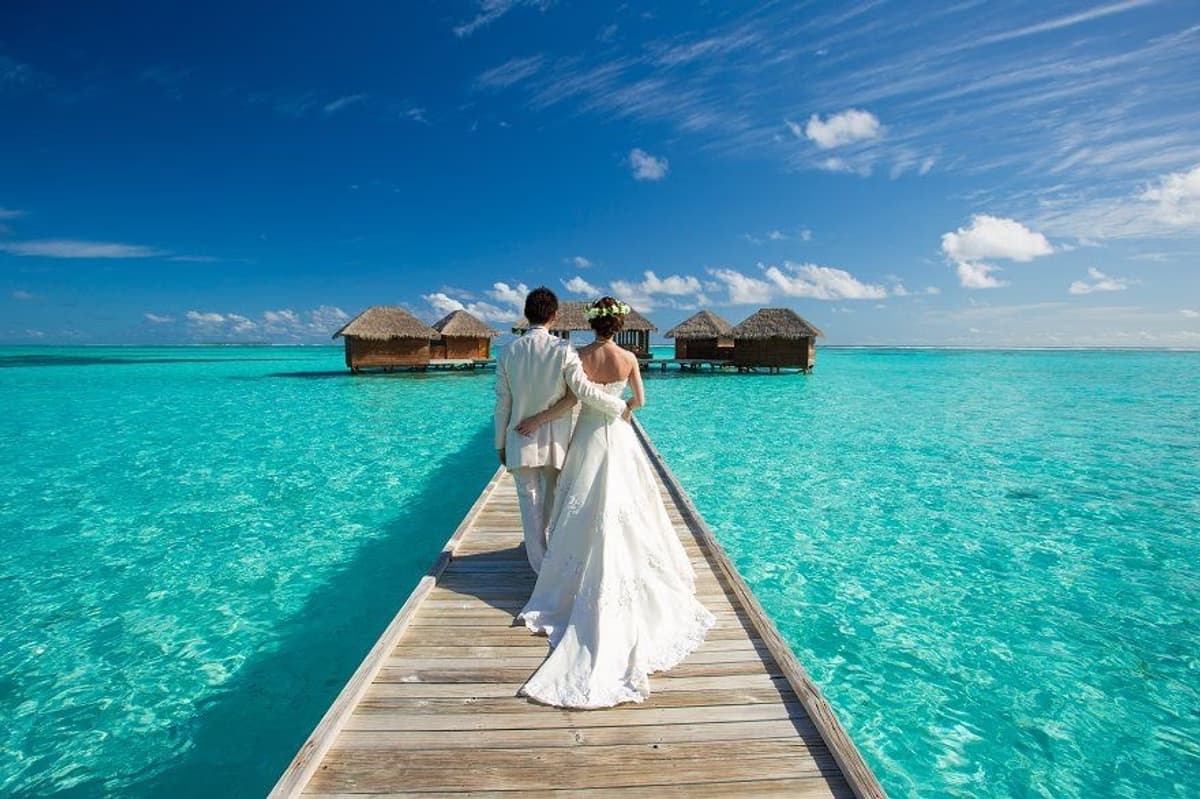 Bride and groom walking the jetty to overwater villas in the Maldives, destination wedding makeup by Elani Artistry