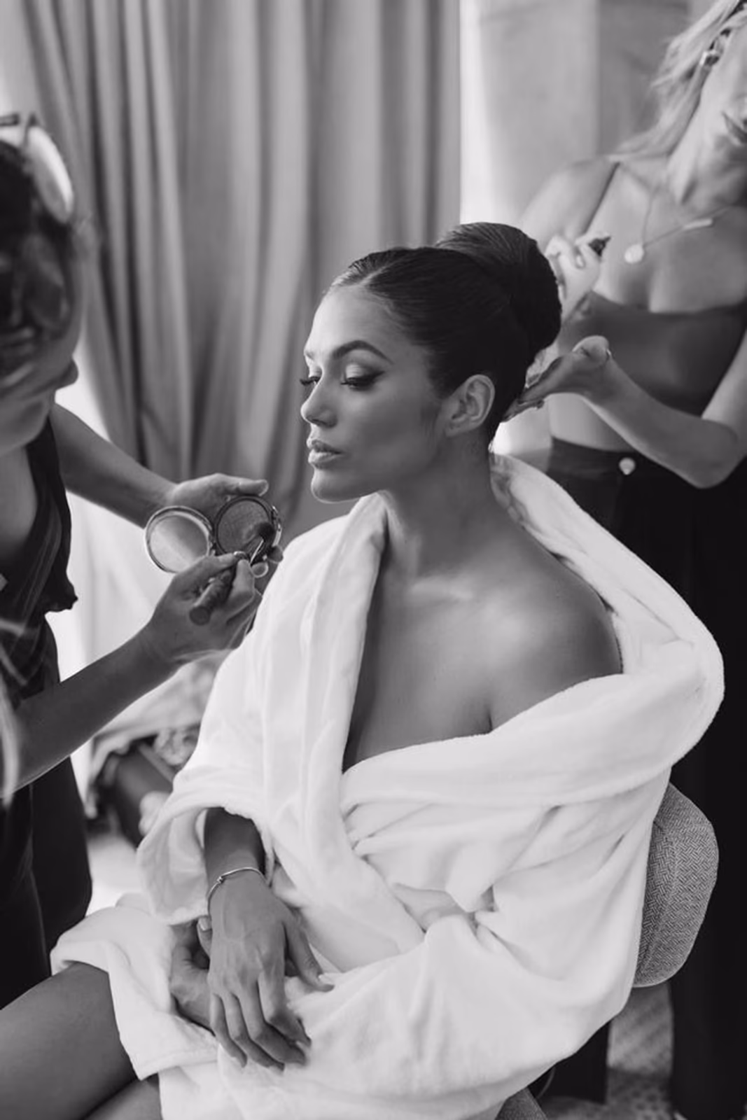 Bride getting final touches of makeup applied while seated in a robe, black and white bridal getting ready photo by Elani Artistry Dubai